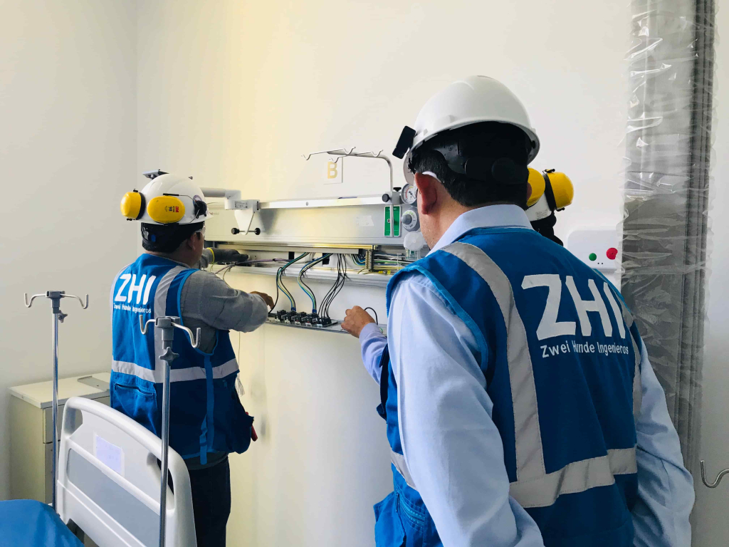 Ingenieros de ZHI realizando instalación y revisión de cabecera hospitalaria con conexiones de gases medicinales en habitación de hospital
